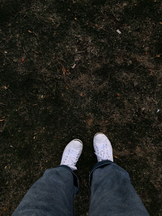 a person standing on top of a grass covered field, a picture, wearing white sneakers, low quality photograph, dark photo, looking down at you