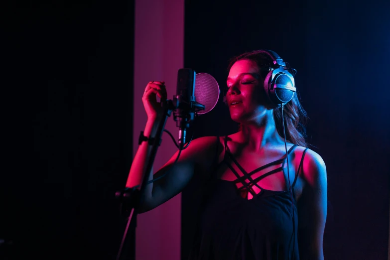 a woman singing into a microphone with headphones on, an album cover, by Julia Pishtar, pexels, studio lighting 4 k, avatar image, behind the scenes, modeled