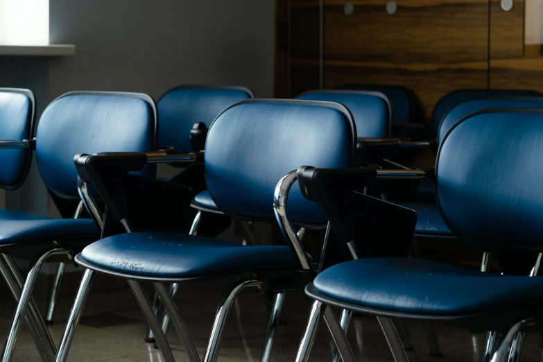 a group of blue chairs sitting next to each other, a portrait, by Jesper Knudsen, trending on unsplash, paris school, background image, blackboard in background, ignant, hoyte van hoytema