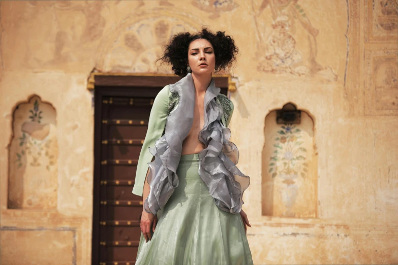 a woman in a green dress standing in front of a building, renaissance, haute couture fashion shoot, wearing jedi robes and a sari, wearing jacket and skirt, muted pastels