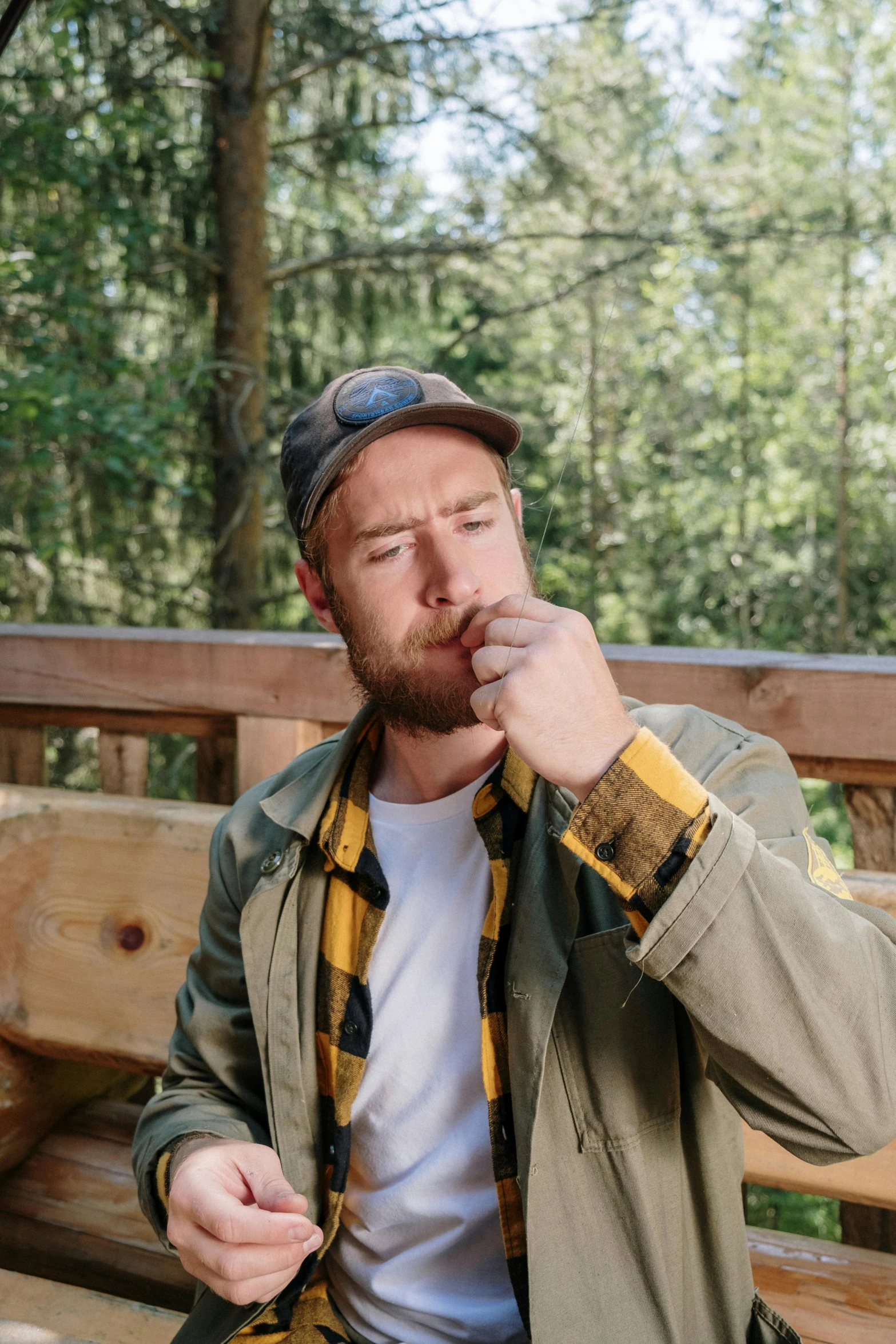 a man sitting on top of a wooden bench, smoking a joint, reddish beard, in front of a forest background, casey cooke