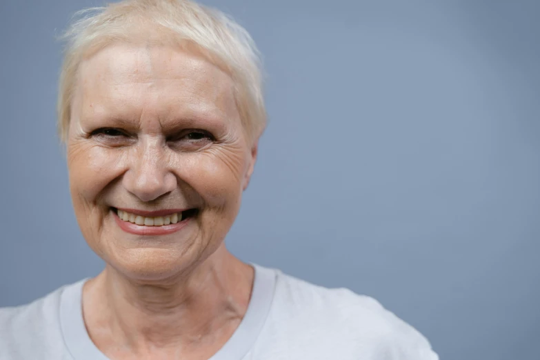 a close up of a person with a smile on their face, older woman, solid background, pale grey skin, symetrical facial