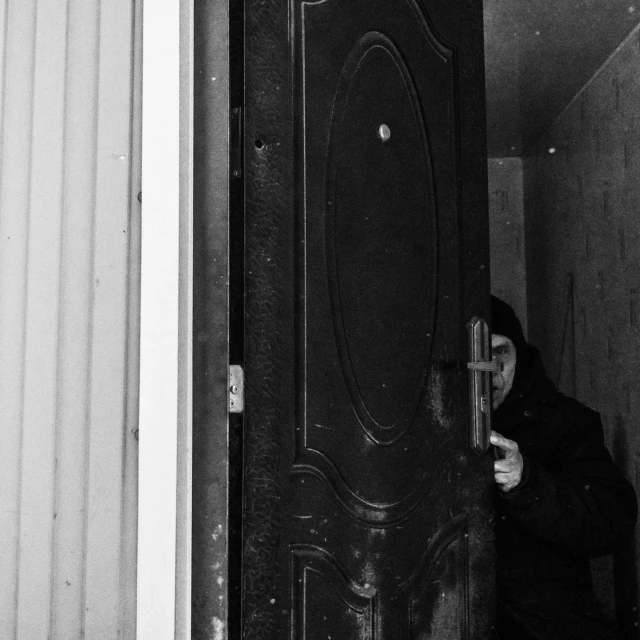 a black and white photo of a person standing in front of a door, a black and white photo, unsplash, surrealism, soviet apartment, selfie, hunting, unknown artist