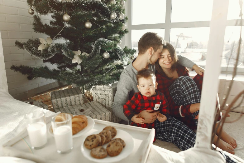 a family sitting on a bed in front of a christmas tree, a photo, pexels, realism, eating, good morning, profile pic, cozy wallpaper