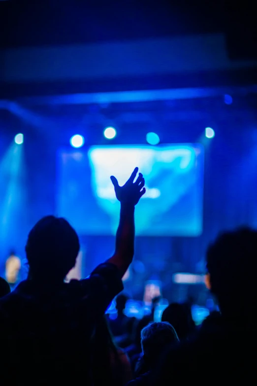 a person raising their hand at a concert, by Dan Content, pexels, holding a holy symbol, brightly lit blue room, scene from church, ilustration