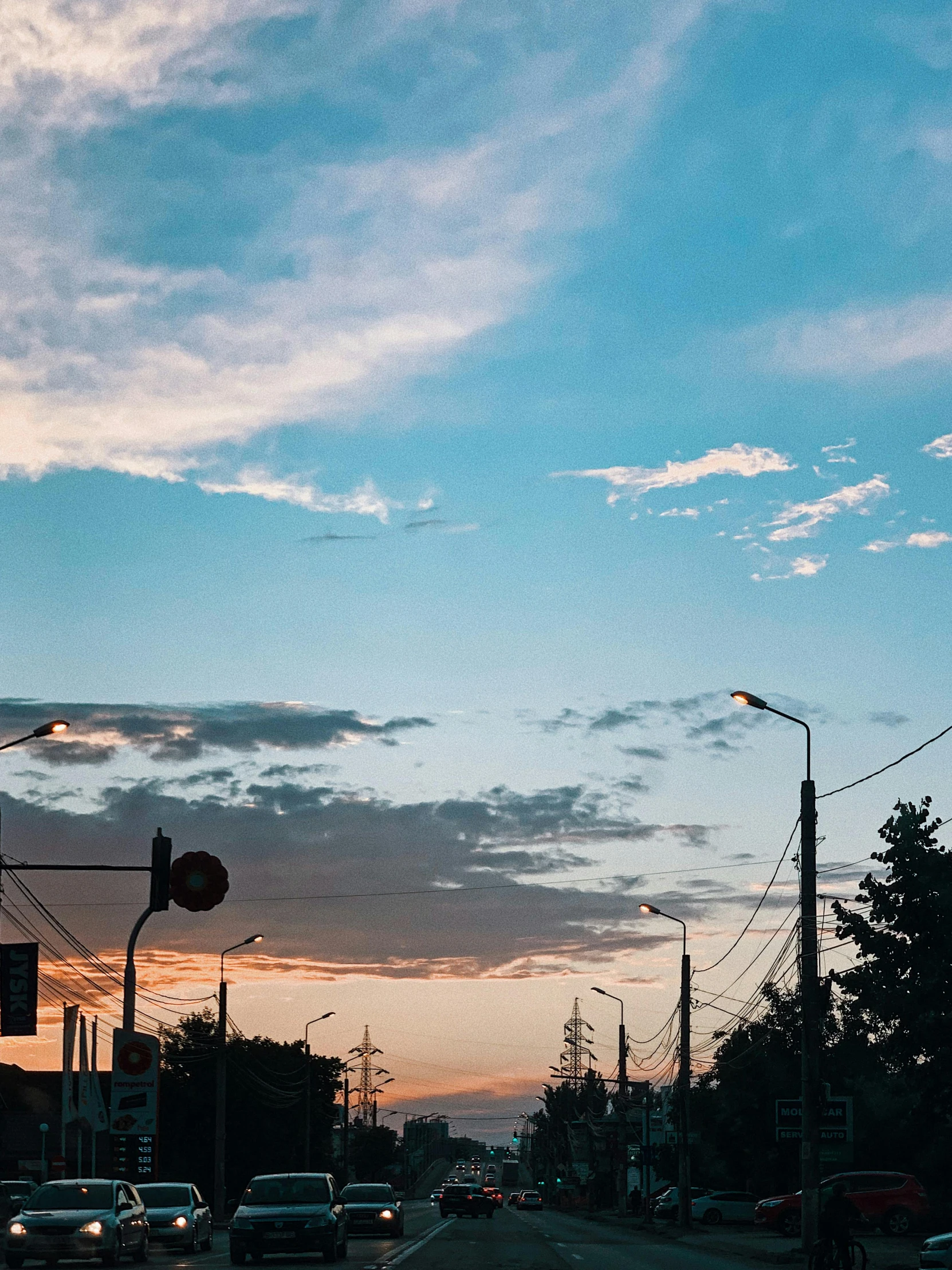 a street filled with lots of traffic next to tall buildings, an album cover, unsplash contest winner, aestheticism, beautiful dusk sky, magical soviet town, power lines, ((sunset))