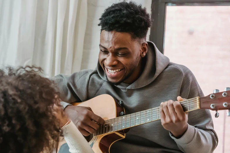 a man sitting on a couch playing a guitar, pexels contest winner, black arts movement, caring fatherly wide forehead, brown skin man with a giant grin, women playing guitar, black teenage boy