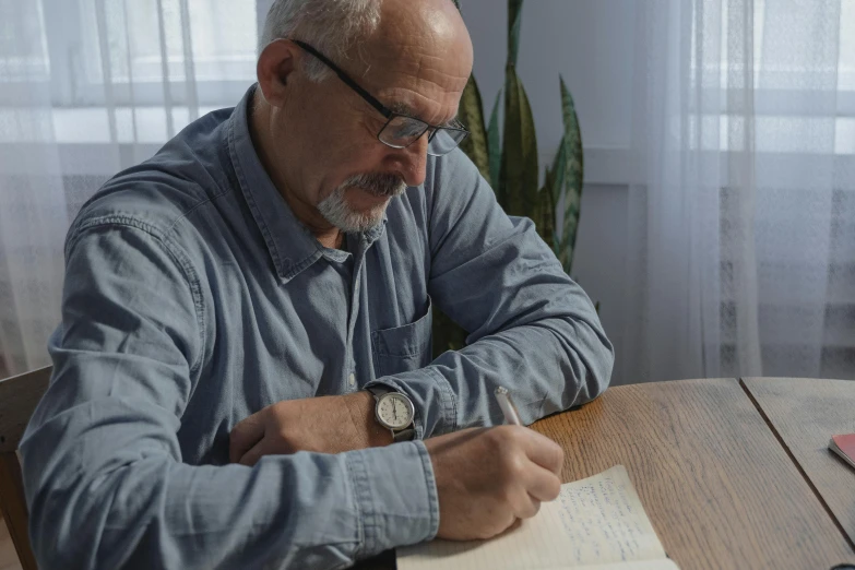 a man sitting at a table writing on a piece of paper, lynn skordal, profile image, portrait image, cinematic image