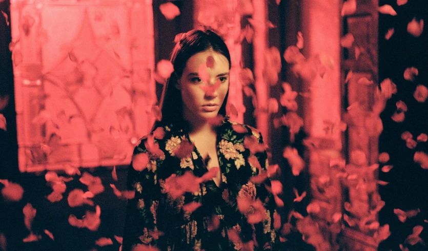 a woman standing in a room surrounded by petals, an album cover, inspired by Elsa Bleda, pexels contest winner, serial art, red lighting on their faces, hailee steinfeld, grainy movie still, orelsan
