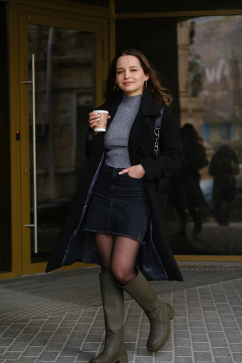 a woman walking down a sidewalk with a cup of coffee, style of julia razumova, mackenzie foy, knee-high boots, neo kyiv