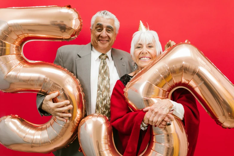 a man and a woman holding balloons in front of a red background, by Edward Avedisian, pexels contest winner, renaissance, elderly, golden number, 15081959 21121991 01012000 4k, photo booth