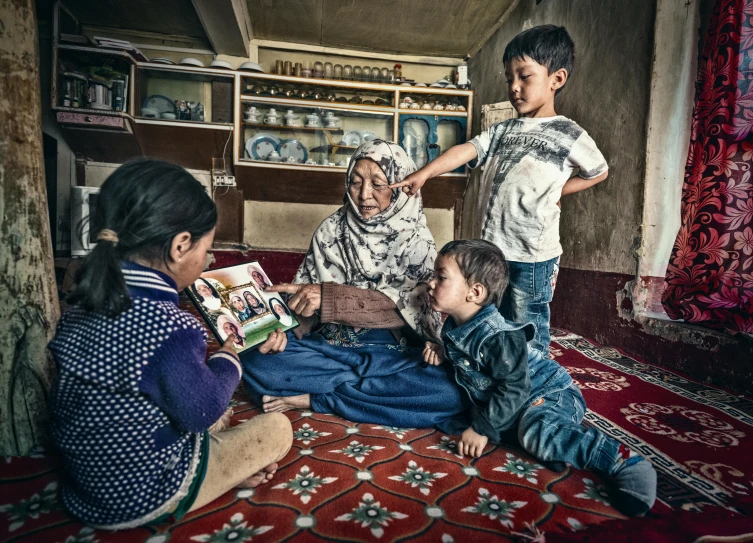 a group of children sitting on top of a rug, a portrait, by Ibrahim Kodra, pexels contest winner, an elderly, small library, sitting in rural living room, thumbnail