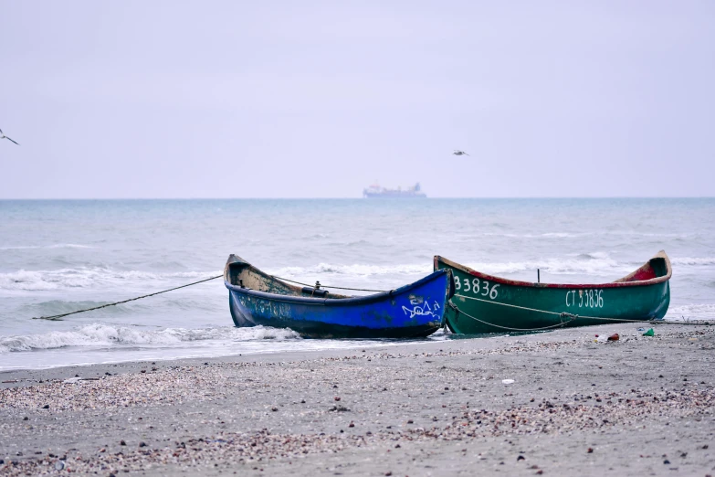 a couple of boats sitting on top of a sandy beach, unsplash, visual art, dunkirk, profile image, blue and purple and green, black sea