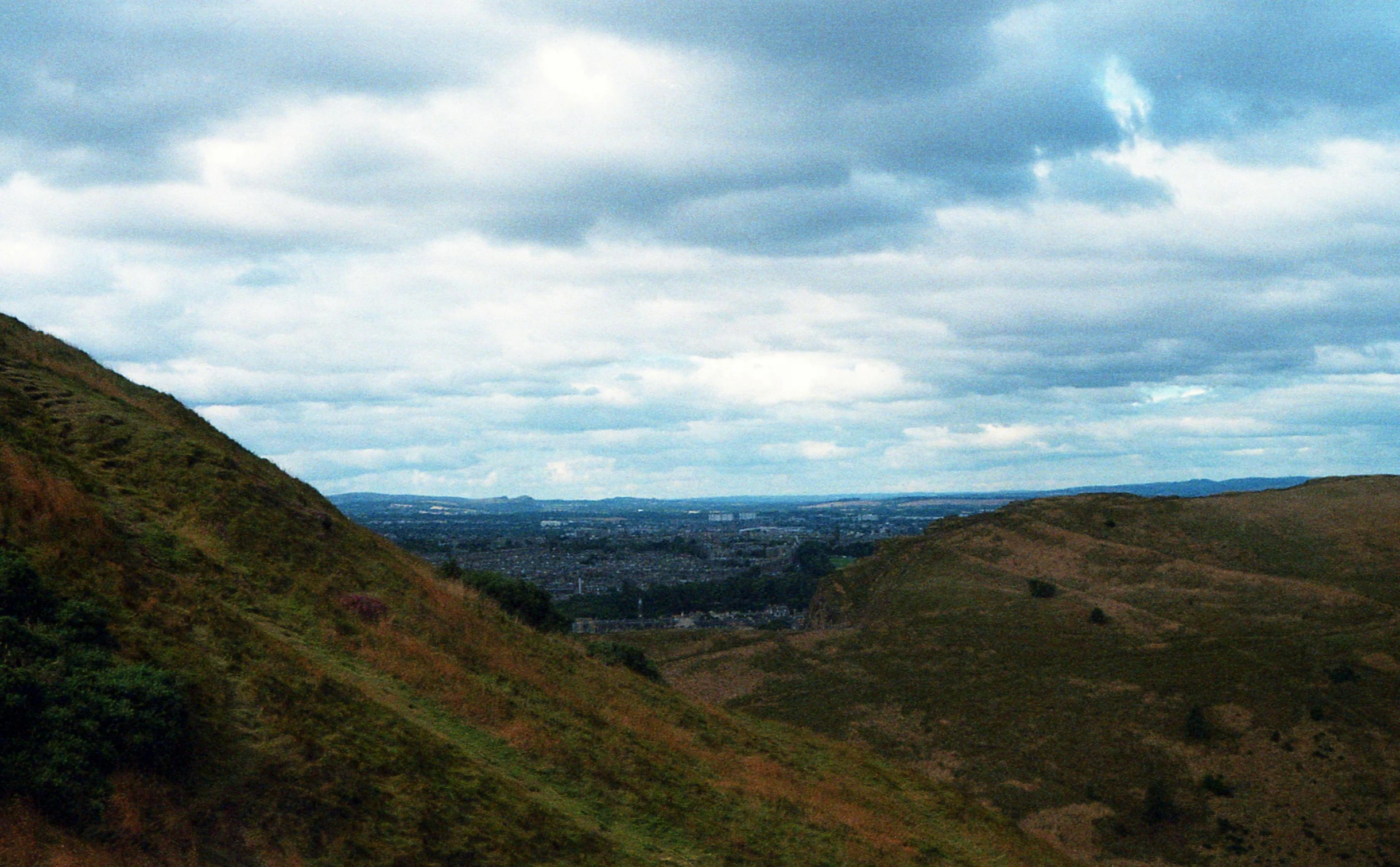 a view of a city from the top of a hill, an album cover, inspired by Thomas Struth, unsplash, moorland, paisley, lush valley, blue