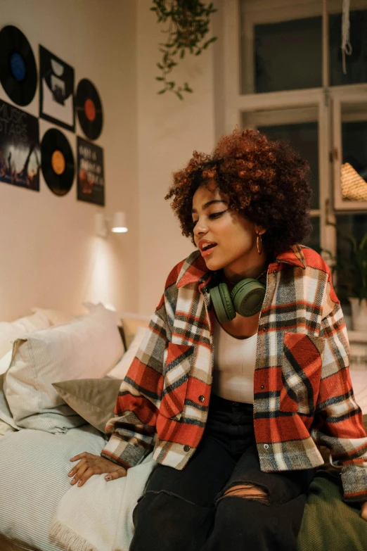 a woman sitting on a bed wearing headphones, trending on pexels, funk art, wearing a plaid shirt, afro tech, inside a cozy apartment, wearing a fancy jacket