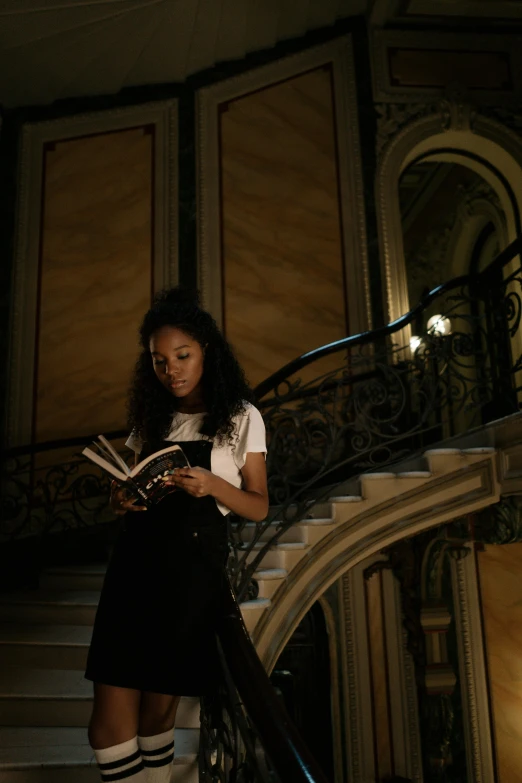 a woman standing on a set of stairs reading a book, pexels contest winner, renaissance, dark skinned, [ theatrical ], inside a grand, vanessa morgan