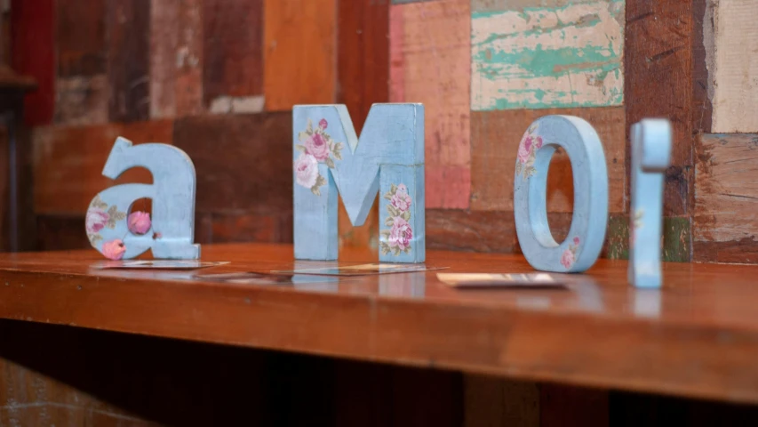 a couple of wooden letters sitting on top of a table, by Alice Mason, unsplash, cloisonnism, meow, floral motives, homely atmosphere, motherly