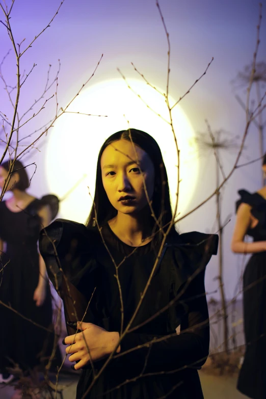 a woman in a black dress standing in front of a full moon, an album cover, inspired by Qian Xuan, pose 1 of 1 6, triad of muses, looking towards camera, still from a music video