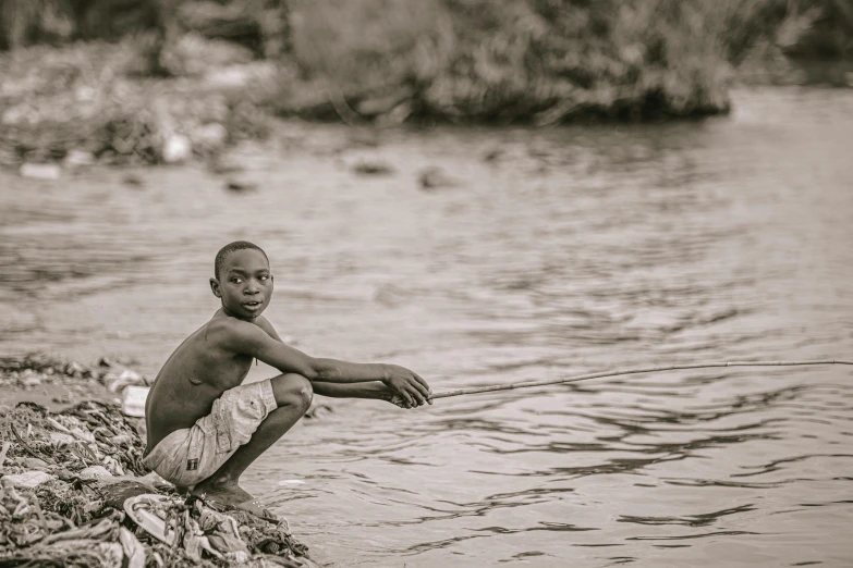 a boy sitting on a rock next to a body of water, by Chinwe Chukwuogo-Roy, pexels contest winner, process art, with grey skin, small river, childish gambino, water eyes