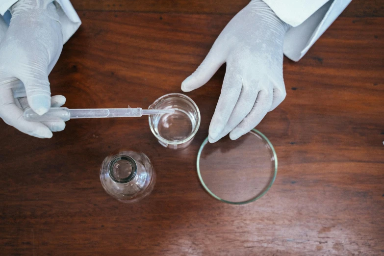 a person in white gloves holding a glass with a liquid in it, hand on table, magnifying glass, thumbnail, white