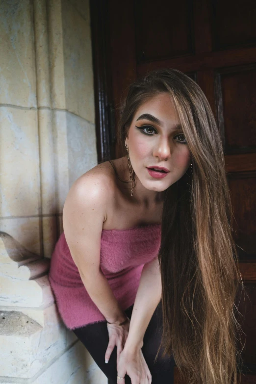 a woman with long hair leaning against a wall, a picture, trending on pexels, wearing a pink dress, asher duran, her skin is light brown, portrait of modern darna