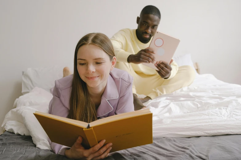 a girl laying on a bed reading a book, pexels contest winner, happening, medium shot of two characters, with yellow cloths, 30 year old man, with a white complexion
