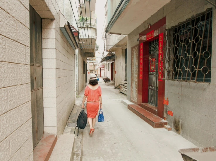 a woman in an orange dress walking down a narrow street, an album cover, inspired by Zhang Kechun, pexels contest winner, mingei, outlive streetwear collection, porcelain skin ”, subtitles, red dress and hat