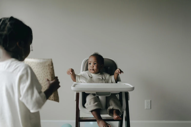 a woman standing next to a baby in a high chair, pexels contest winner, dark-skinned, 1 2 9 7, in a comfortable chair, low quality photo