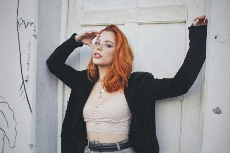 a woman with red hair leaning against a wall, inspired by Elsa Bleda, pexels contest winner, better known as amouranth, sydney sweeney, black and orange, on a pale background