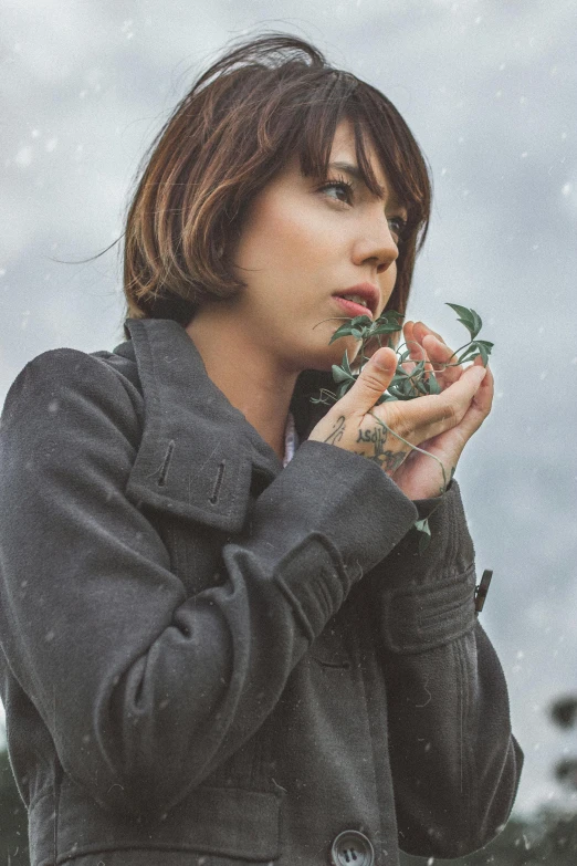 a woman standing in the snow holding a flower, a colorized photo, inspired by Elsa Bleda, trending on pexels, portrait of max caulfield, aubrey plaza, covered in plants, thoughtful )