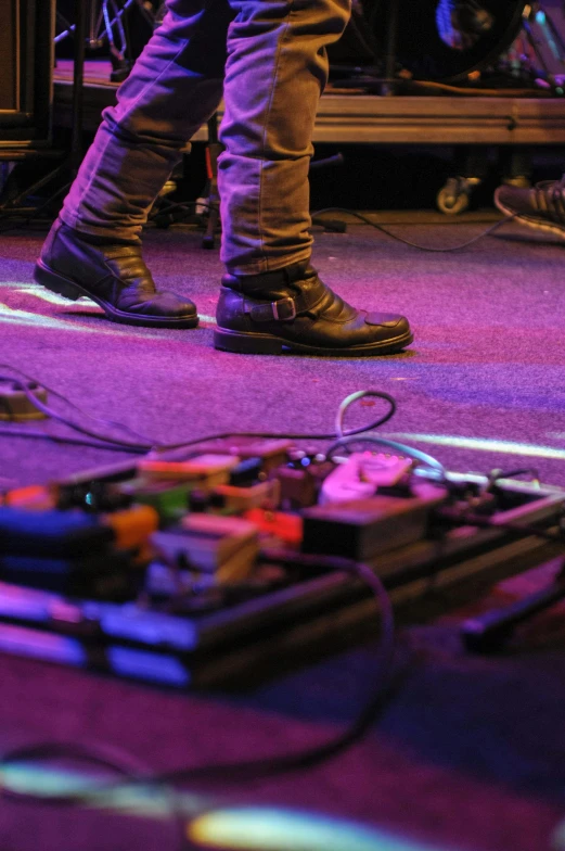 a person standing on a stage with a guitar, by Jesse Richards, pexels, happening, cables on floor, inputs, shoes, great details