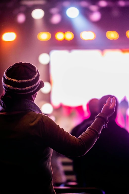 a woman standing in front of a crowd at a concert, pexels, happening, holding a holy symbol, vibrant backlit, contemplating, a colorful
