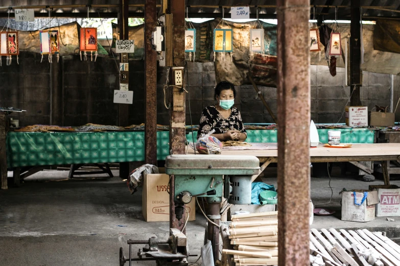 a woman sitting at a table working on a piece of wood, a portrait, trending on unsplash, cloisonnism, fish market stalls, wearing a mask, “ full body, conde nast traveler photo