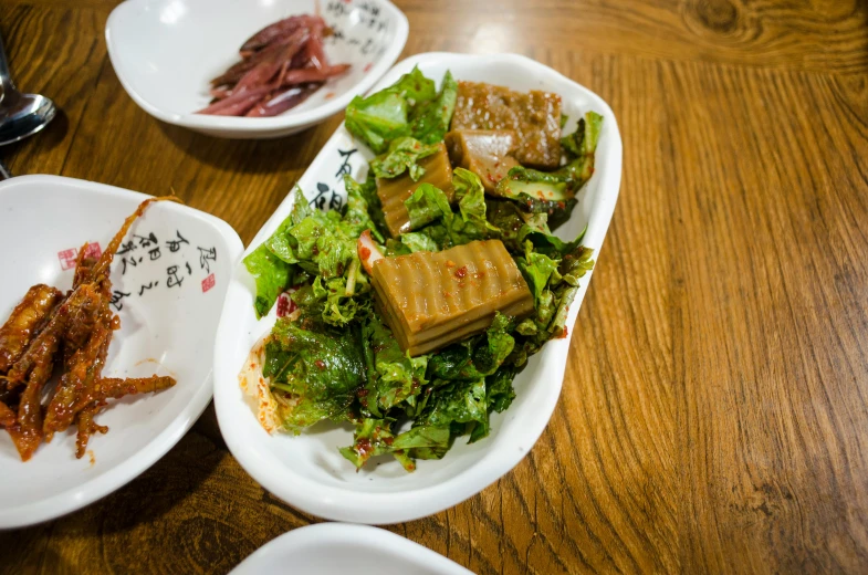 a wooden table topped with plates of food, a picture, unsplash, mingei, lettuce, square, well preserved, brown