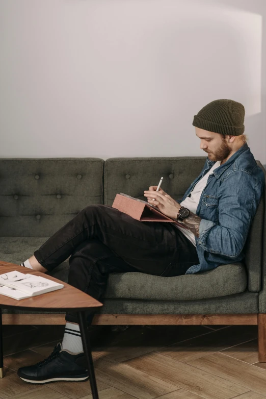 a man sitting on a couch reading a book, a drawing, trending on pexels, writing in journal, casually dressed, tattooed, promotional image
