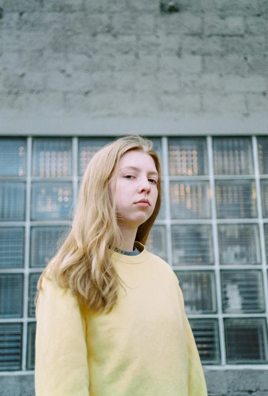 a woman standing in front of a building, unsplash, hyperrealism, medium yellow blond hair, she is about 1 6 years old, plain background, low quality photo