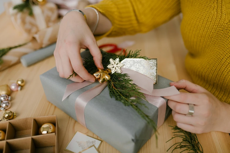 a woman wrapping a christmas present on a table, by Eden Box, pexels contest winner, arts and crafts movement, grey and silver, golden ribbon, overview, bows