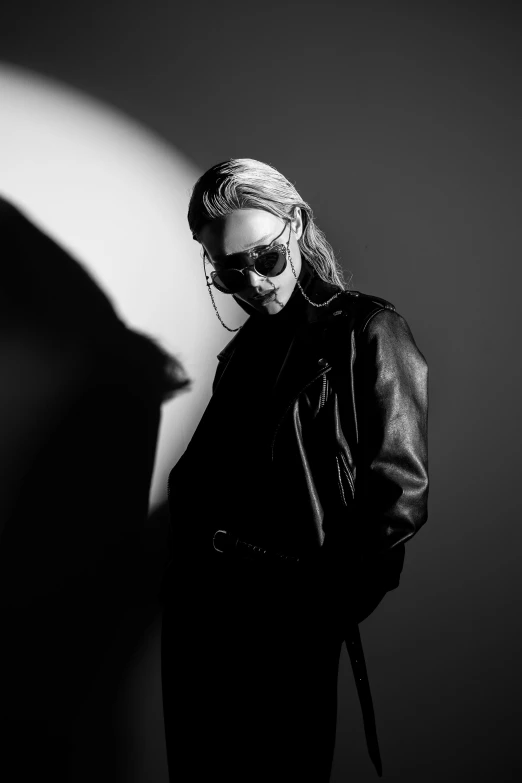 a black and white photo of a woman in a coat and sunglasses, a black and white photo, by Clifford Ross, trending on pexels, neon operator margot robbie, she wears leather jacket, studio lit, johan liebert