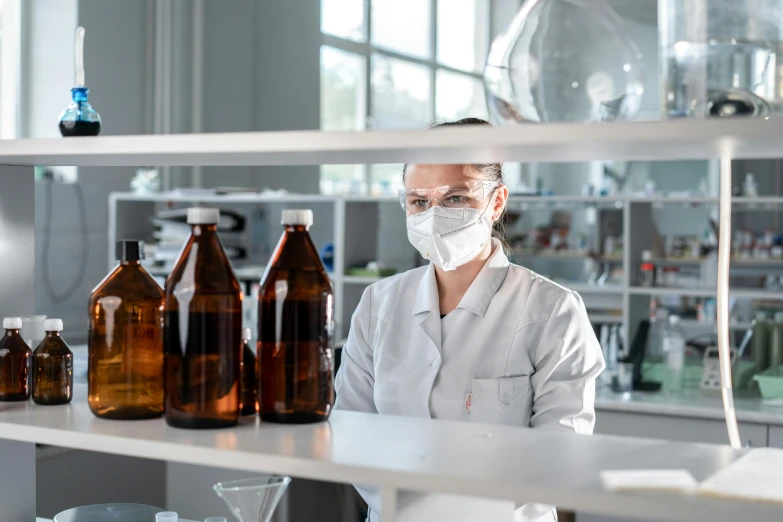 a woman wearing a face mask in a laboratory, by Adam Marczyński, pexels contest winner, holding a bottle of arak, profile image, large jars on shelves, brown