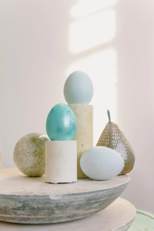 a bowl sitting on top of a wooden table, an abstract sculpture, inspired by Emil Carlsen, new sculpture, translucent eggs, pastel blue, on a candle holder, various sizes