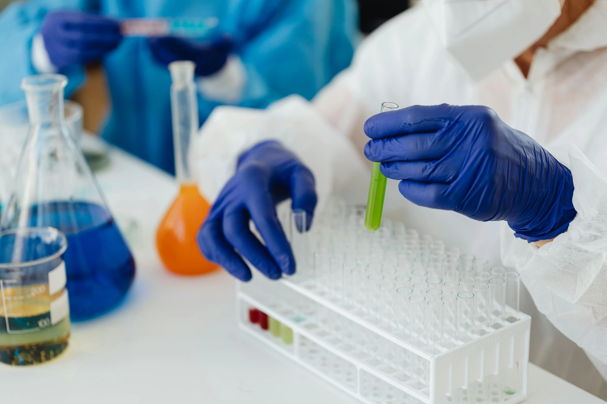 a person in a lab coat holding a test tube, chartreuse and orange and cyan, gloves on hands, blue and purple and green, person in foreground