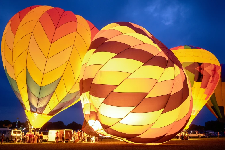 a group of hot air balloons sitting on top of a field, purple and yellow lighting, event photography, orange glow, tie-dye