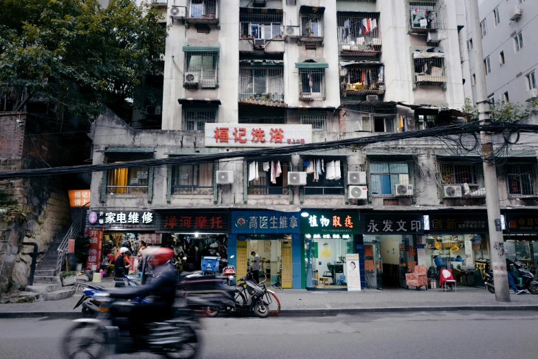 a man riding a motorcycle past a tall building, inspired by Zhang Kechun, unsplash, old shops, lots of shops, a quaint, su fu