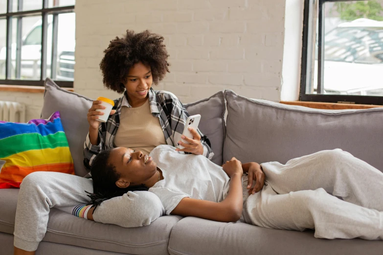 a woman sitting on top of a couch next to a man, trending on pexels, lesbians, black teenage girl, integrating with technology, woman holding another woman