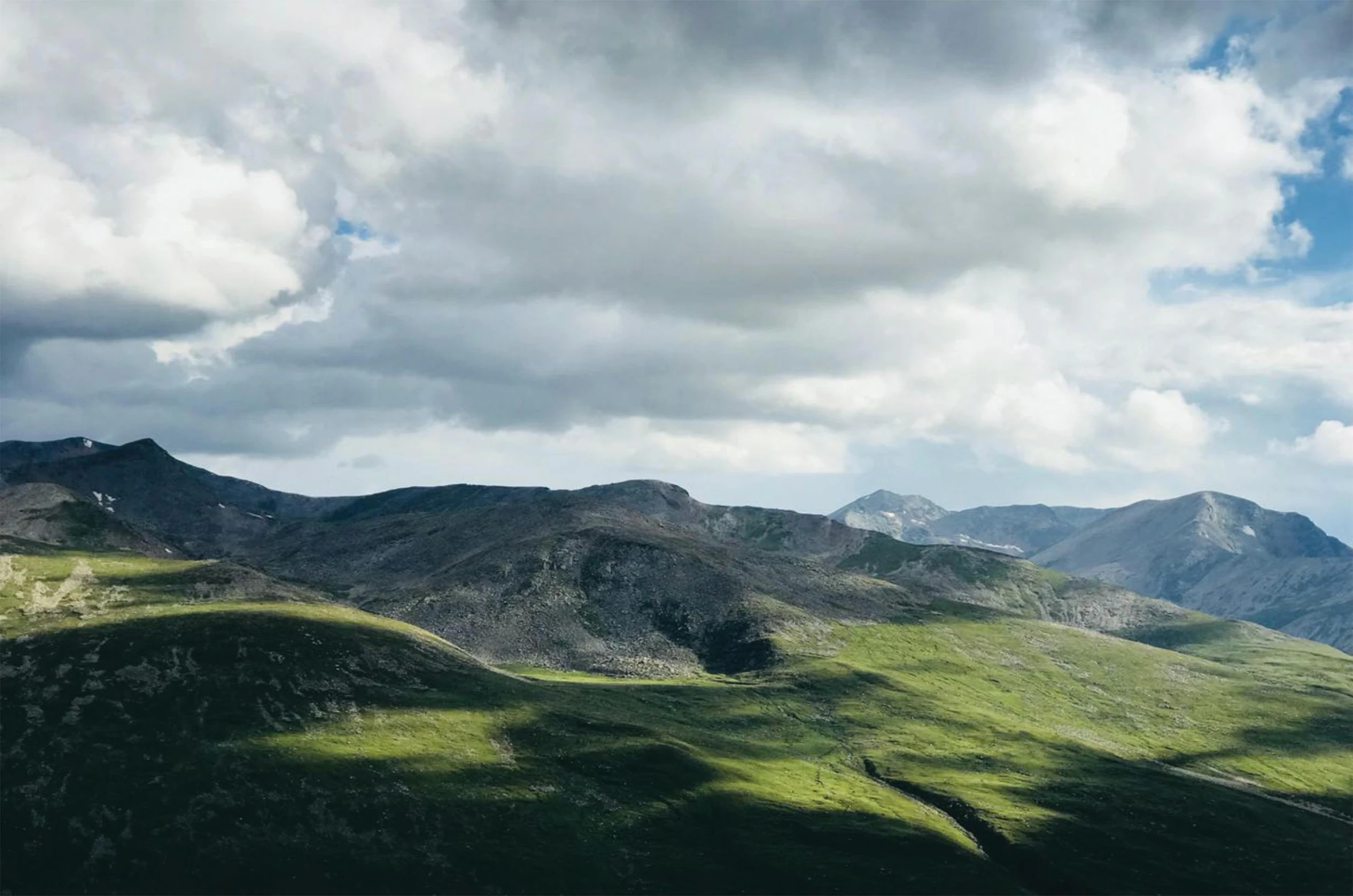 a herd of cattle grazing on top of a lush green hillside, by Bedwyr Williams, unsplash contest winner, grey cloudy skies, “ aerial view of a mountain, panoramic, high quality desktop wallpaper