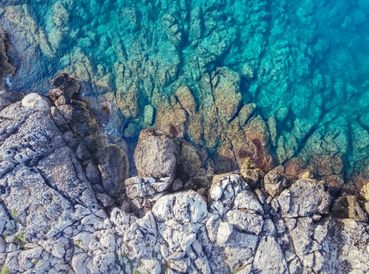 a bird's eye view of some rocks and water, a screenshot, pexels contest winner, mediterranean, crystal clear, contrasting colours, thumbnail