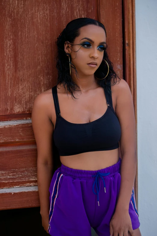 a woman standing in front of a wooden door, an album cover, inspired by Esaias Boursse, trending on pexels, detailed sports bra, black and purple, black teenage girl, indian