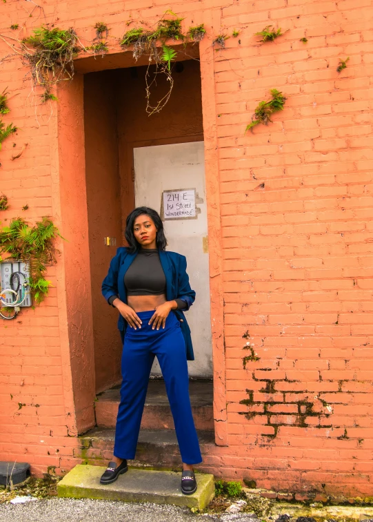 a woman standing in front of a brick building, blue pants, r&b, vibrant aesthetic, 2019 trending photo