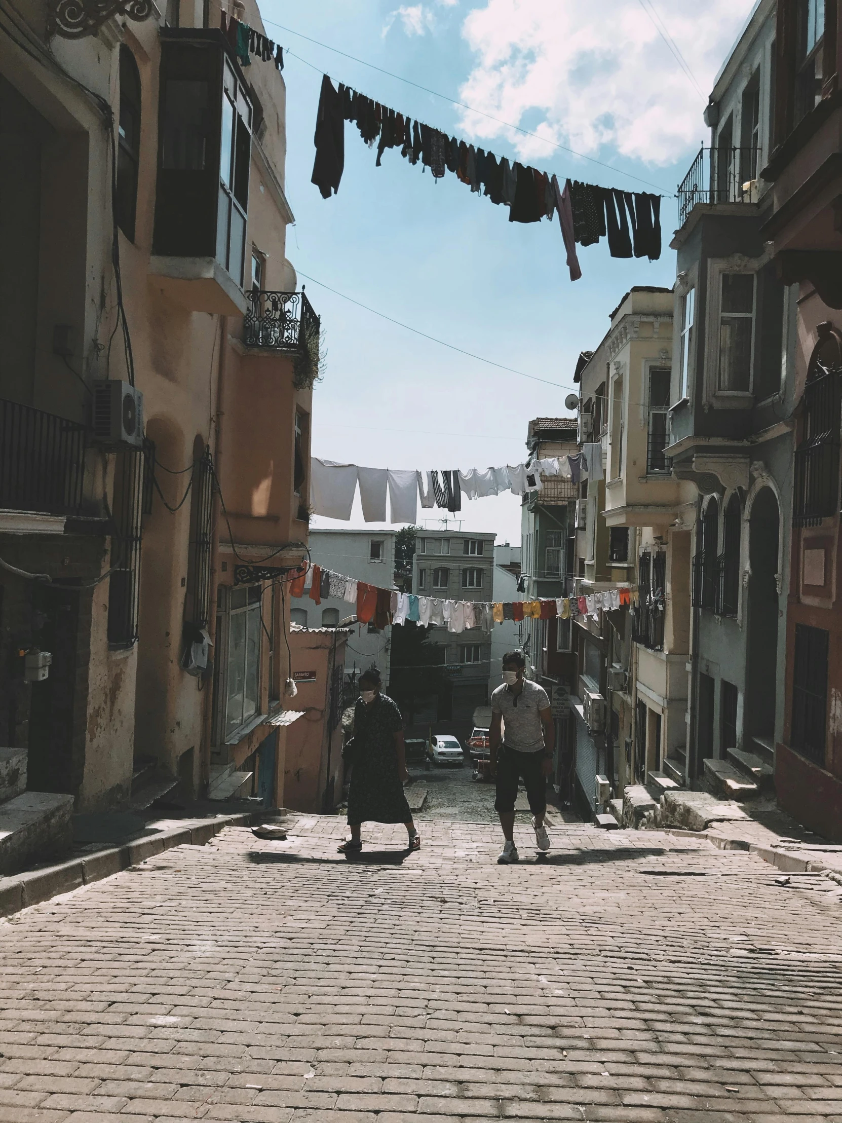 a couple of people walking down a cobblestone street, by Lucia Peka, pexels contest winner, fallout style istanbul, built on a steep hill, gif, bright summer day
