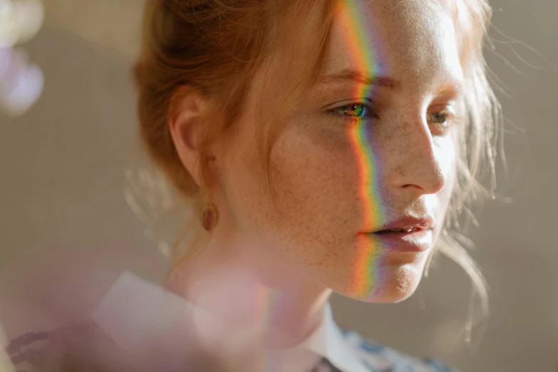 a close up of a woman with freckles on her face, inspired by Gabriel Dawe, trending on pexels, light and space, rainbow reflection, a redheaded young woman, standing under a beam of light, near a window